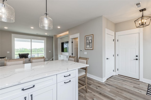 kitchen with a breakfast bar, white cabinetry, light stone counters, light wood-type flooring, and pendant lighting