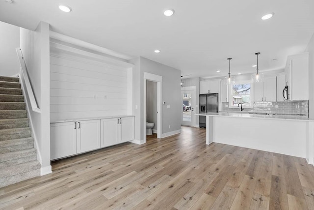 kitchen with pendant lighting, white cabinetry, backsplash, stainless steel appliances, and light wood-type flooring