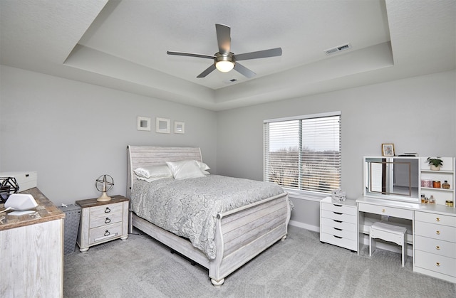 carpeted bedroom with ceiling fan and a tray ceiling