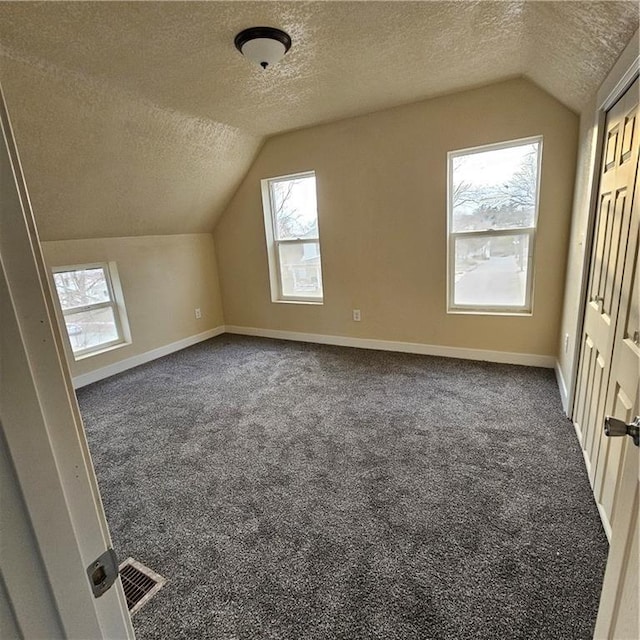 bonus room featuring vaulted ceiling, a textured ceiling, and dark colored carpet