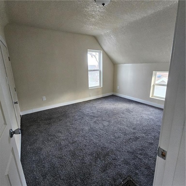 bonus room featuring dark carpet, vaulted ceiling, and a textured ceiling