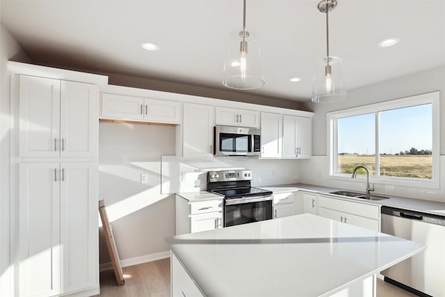 kitchen featuring a kitchen island, appliances with stainless steel finishes, sink, white cabinets, and hanging light fixtures