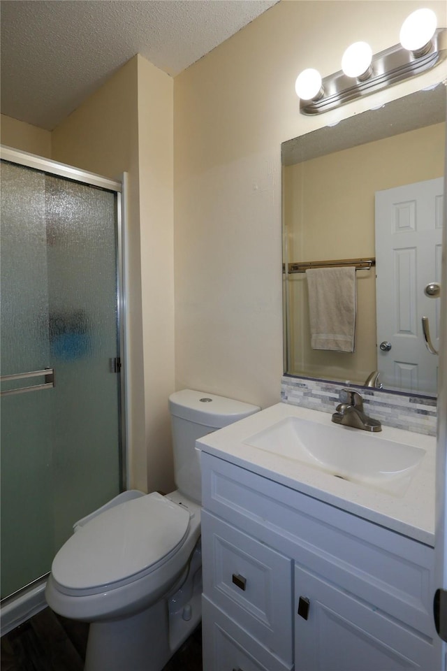 bathroom with vanity, toilet, a textured ceiling, and a shower with shower door