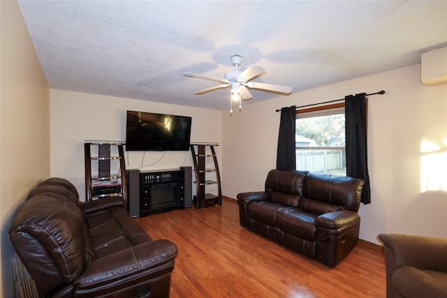 living room featuring hardwood / wood-style flooring, a wall mounted AC, a fireplace, and ceiling fan