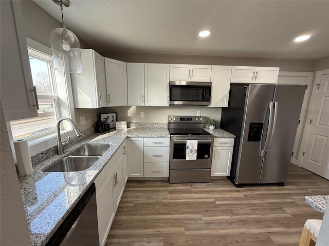 kitchen with a sink, white cabinets, light stone counters, and stainless steel appliances