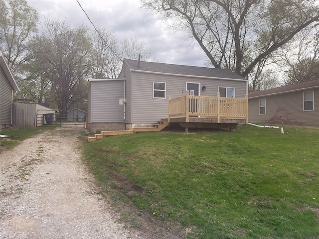 back of property with a lawn, a gate, dirt driveway, and a wooden deck