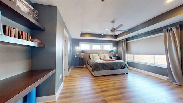 bedroom with light hardwood / wood-style flooring, a raised ceiling, and ceiling fan