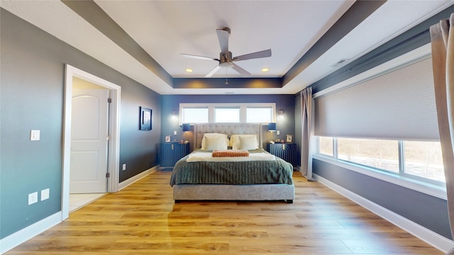 bedroom with a tray ceiling, ceiling fan, and light wood-type flooring