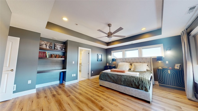 bedroom with ceiling fan, a raised ceiling, and light wood-type flooring