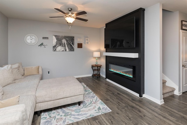 living room featuring ceiling fan, a large fireplace, and dark hardwood / wood-style floors