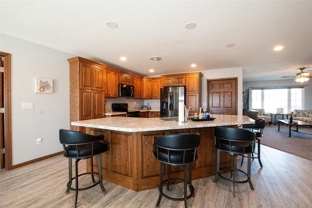 kitchen with appliances with stainless steel finishes, light hardwood / wood-style floors, a breakfast bar area, and a large island with sink