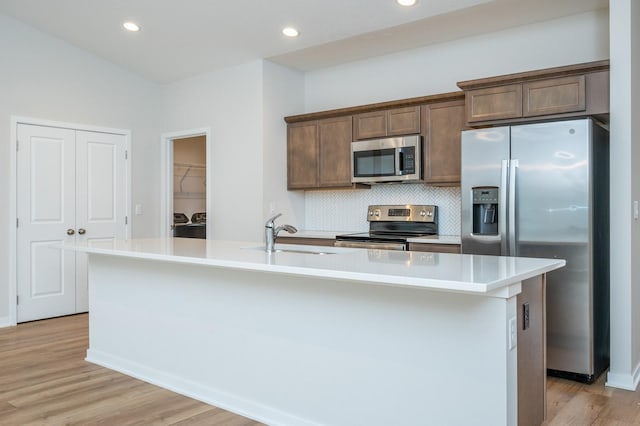 kitchen featuring sink, appliances with stainless steel finishes, tasteful backsplash, light hardwood / wood-style floors, and a center island with sink