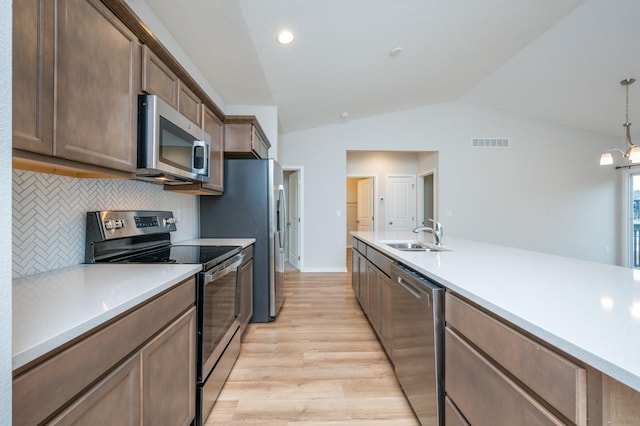 kitchen with lofted ceiling, sink, appliances with stainless steel finishes, backsplash, and hanging light fixtures