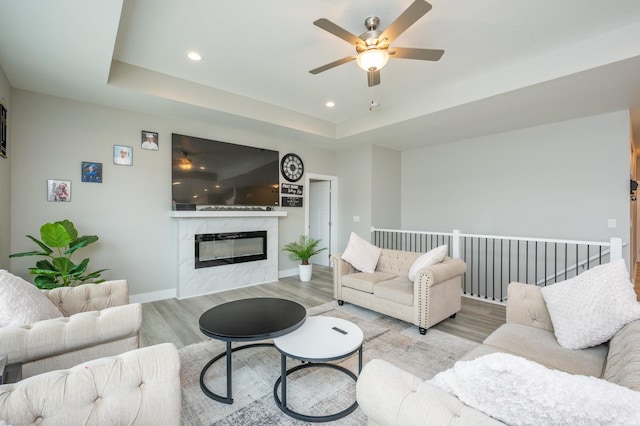 living room featuring ceiling fan, a premium fireplace, a tray ceiling, and light wood-type flooring