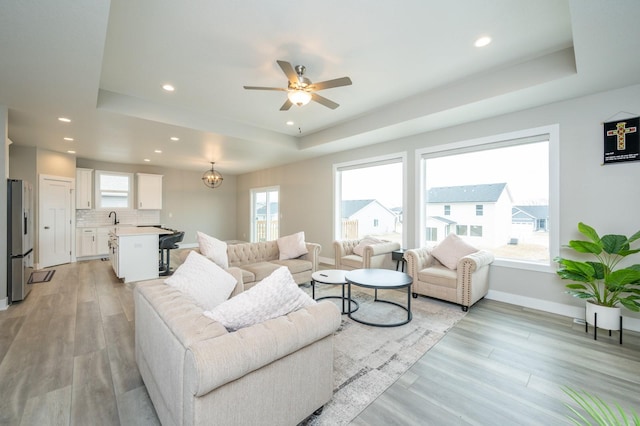 living room with sink, a tray ceiling, light hardwood / wood-style floors, and ceiling fan