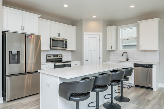 kitchen with a kitchen island, appliances with stainless steel finishes, sink, white cabinets, and light hardwood / wood-style flooring