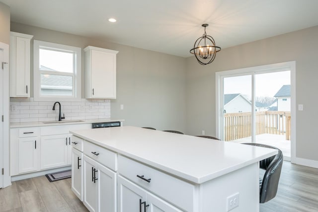 kitchen with decorative light fixtures, sink, white cabinets, a center island, and light hardwood / wood-style flooring