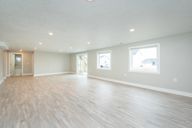 spare room featuring a healthy amount of sunlight, a textured ceiling, and light hardwood / wood-style floors