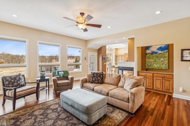 living room featuring a tiled fireplace, ceiling fan with notable chandelier, and dark hardwood / wood-style floors