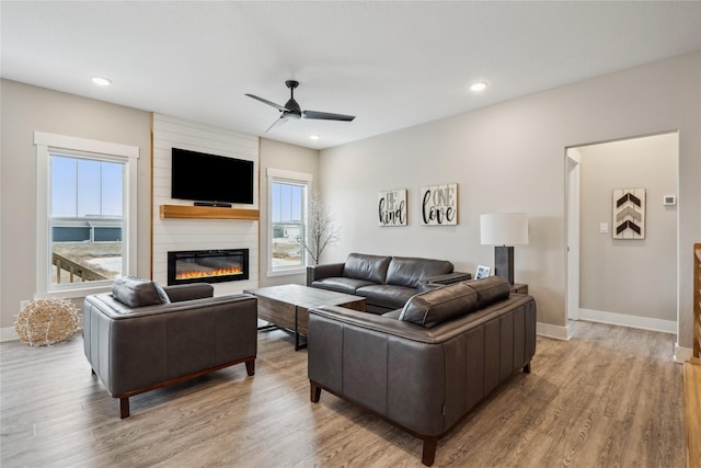 living room featuring ceiling fan, a fireplace, and light hardwood / wood-style floors