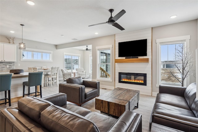 living room with a large fireplace, a healthy amount of sunlight, and light wood-type flooring