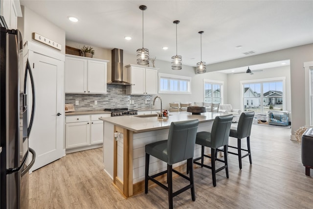 kitchen with wall chimney range hood, decorative light fixtures, stainless steel fridge, and white cabinets