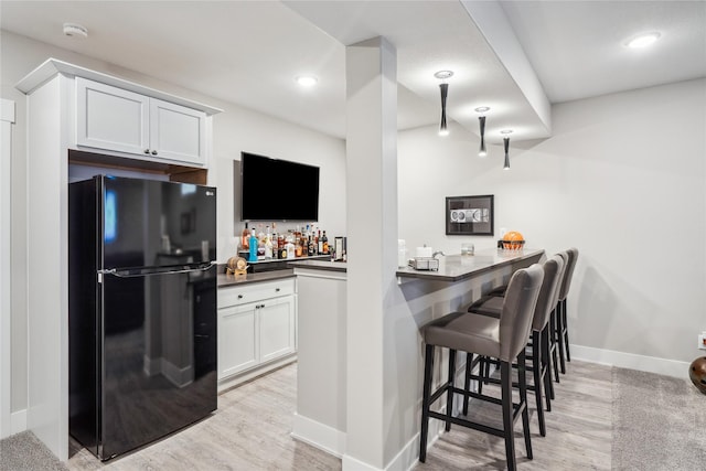 kitchen featuring black refrigerator, white cabinetry, a kitchen breakfast bar, light hardwood / wood-style floors, and kitchen peninsula