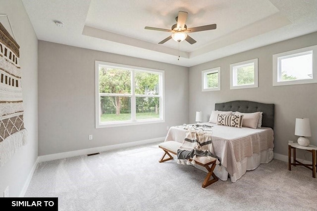 bedroom with a raised ceiling, light carpet, and ceiling fan