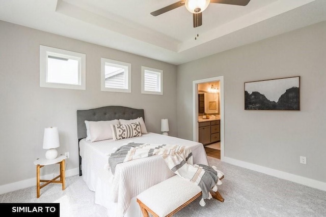 bedroom with light carpet, connected bathroom, a tray ceiling, and ceiling fan