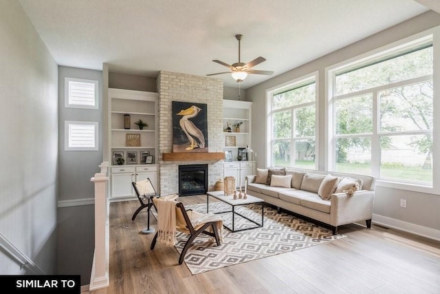 living room featuring built in shelves, ceiling fan, a healthy amount of sunlight, and a fireplace