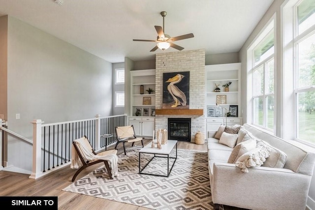 living room with a brick fireplace, built in shelves, a healthy amount of sunlight, and light wood-type flooring