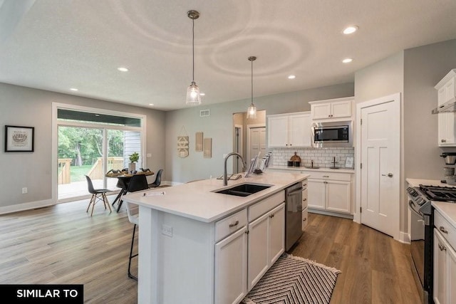 kitchen with sink, white cabinetry, stainless steel appliances, an island with sink, and decorative light fixtures