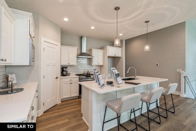 kitchen with a kitchen island with sink, wall chimney range hood, white cabinetry, and sink