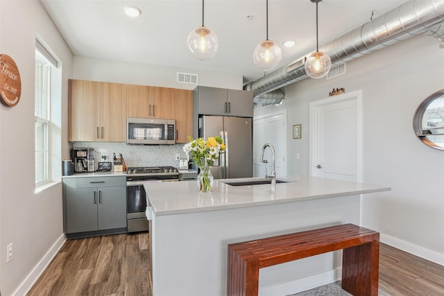 kitchen featuring stainless steel appliances, decorative light fixtures, gray cabinets, and a kitchen island with sink