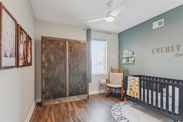 bedroom featuring a crib, wood-type flooring, and ceiling fan