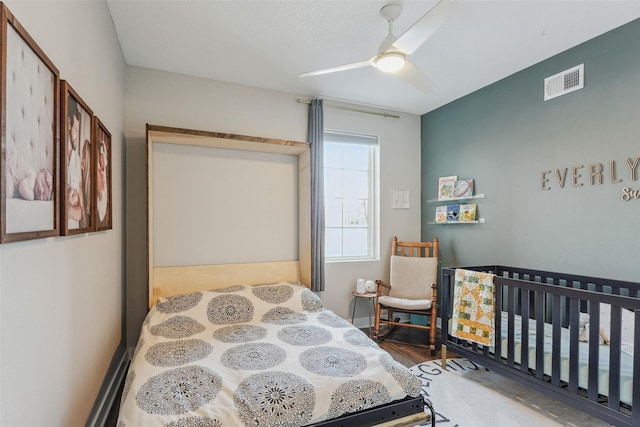 bedroom with hardwood / wood-style flooring, a nursery area, and ceiling fan