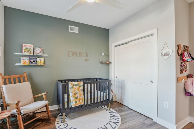 bedroom with wood-type flooring, a crib, a closet, and ceiling fan