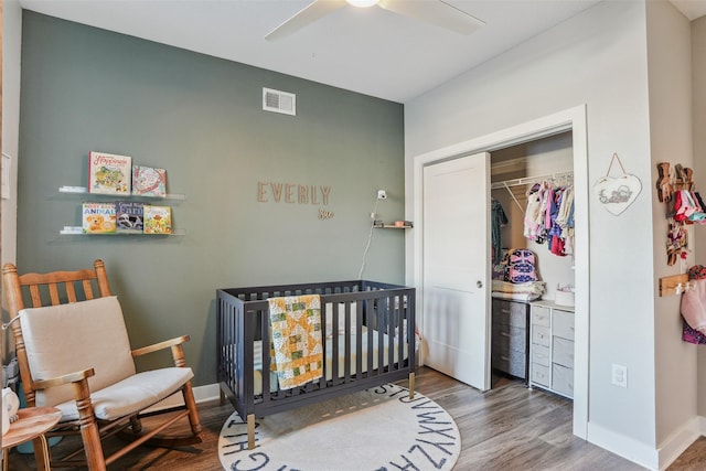 bedroom with a nursery area, ceiling fan, wood-type flooring, and a closet