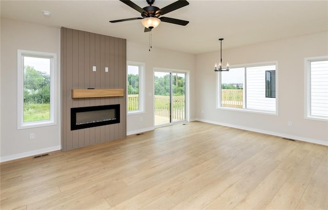 unfurnished living room with a healthy amount of sunlight, a fireplace, ceiling fan with notable chandelier, and light hardwood / wood-style flooring