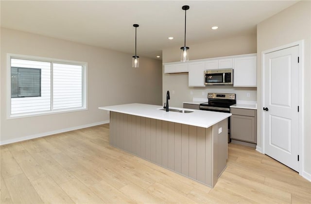 kitchen with sink, decorative light fixtures, a center island with sink, appliances with stainless steel finishes, and light hardwood / wood-style floors