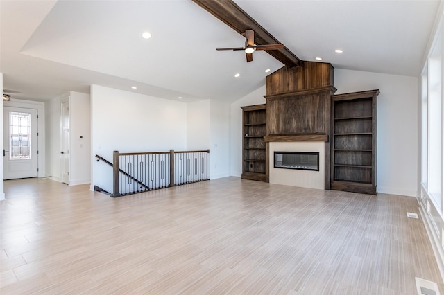 unfurnished living room with vaulted ceiling with beams, a large fireplace, ceiling fan, and light wood-type flooring