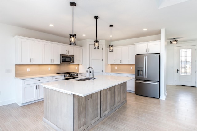 kitchen featuring pendant lighting, sink, a kitchen island with sink, stainless steel appliances, and white cabinets