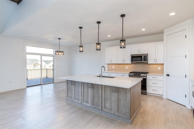 kitchen with sink, white cabinets, backsplash, stainless steel appliances, and a center island with sink