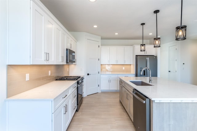 kitchen with sink, decorative light fixtures, an island with sink, stainless steel appliances, and white cabinets