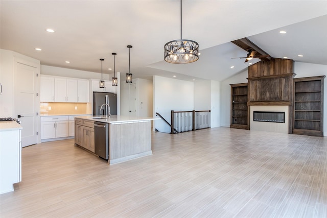 kitchen with appliances with stainless steel finishes, pendant lighting, a fireplace, white cabinetry, and a kitchen island with sink