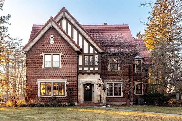 tudor house featuring stone siding, central AC, and a front yard