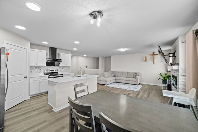 kitchen with appliances with stainless steel finishes, white cabinets, backsplash, wall chimney range hood, and a center island with sink