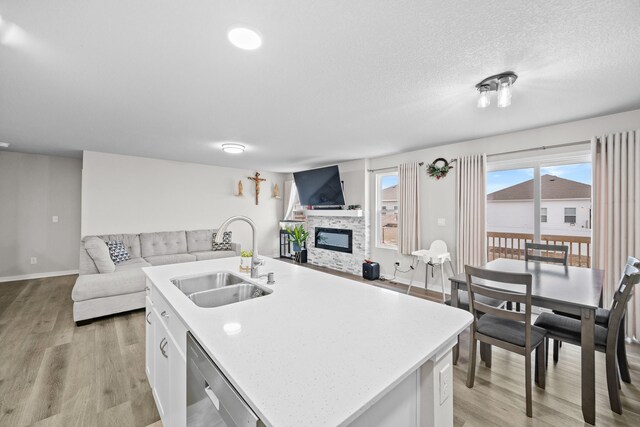 kitchen featuring a fireplace, dishwasher, an island with sink, sink, and white cabinets