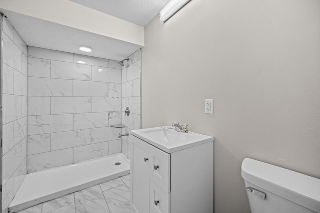 bathroom with tiled shower, vanity, toilet, and a textured ceiling