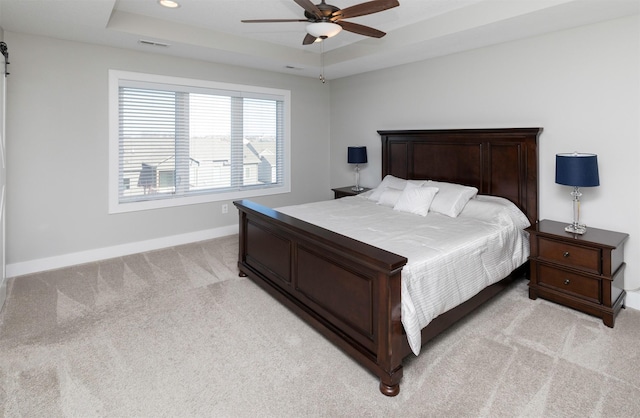 carpeted bedroom with ceiling fan, a barn door, and a raised ceiling